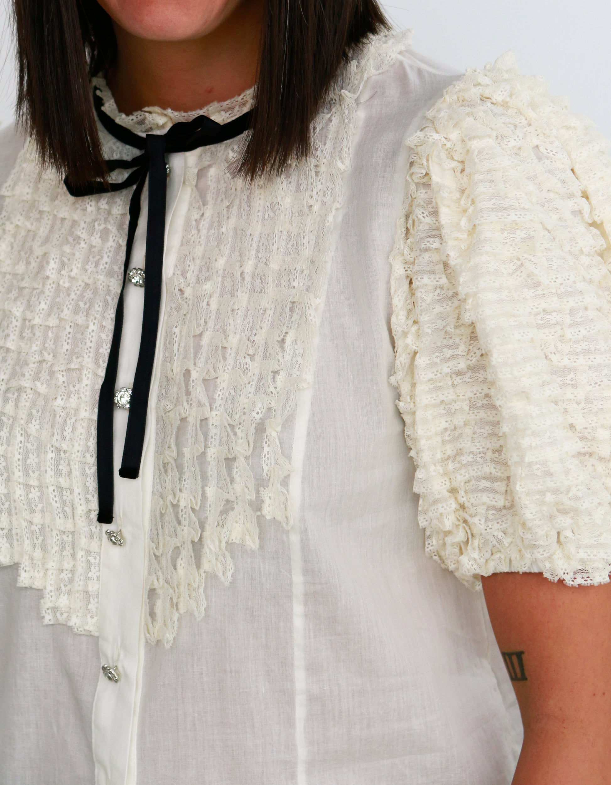 Close-up of a person wearing a white lace blouse with black trim.