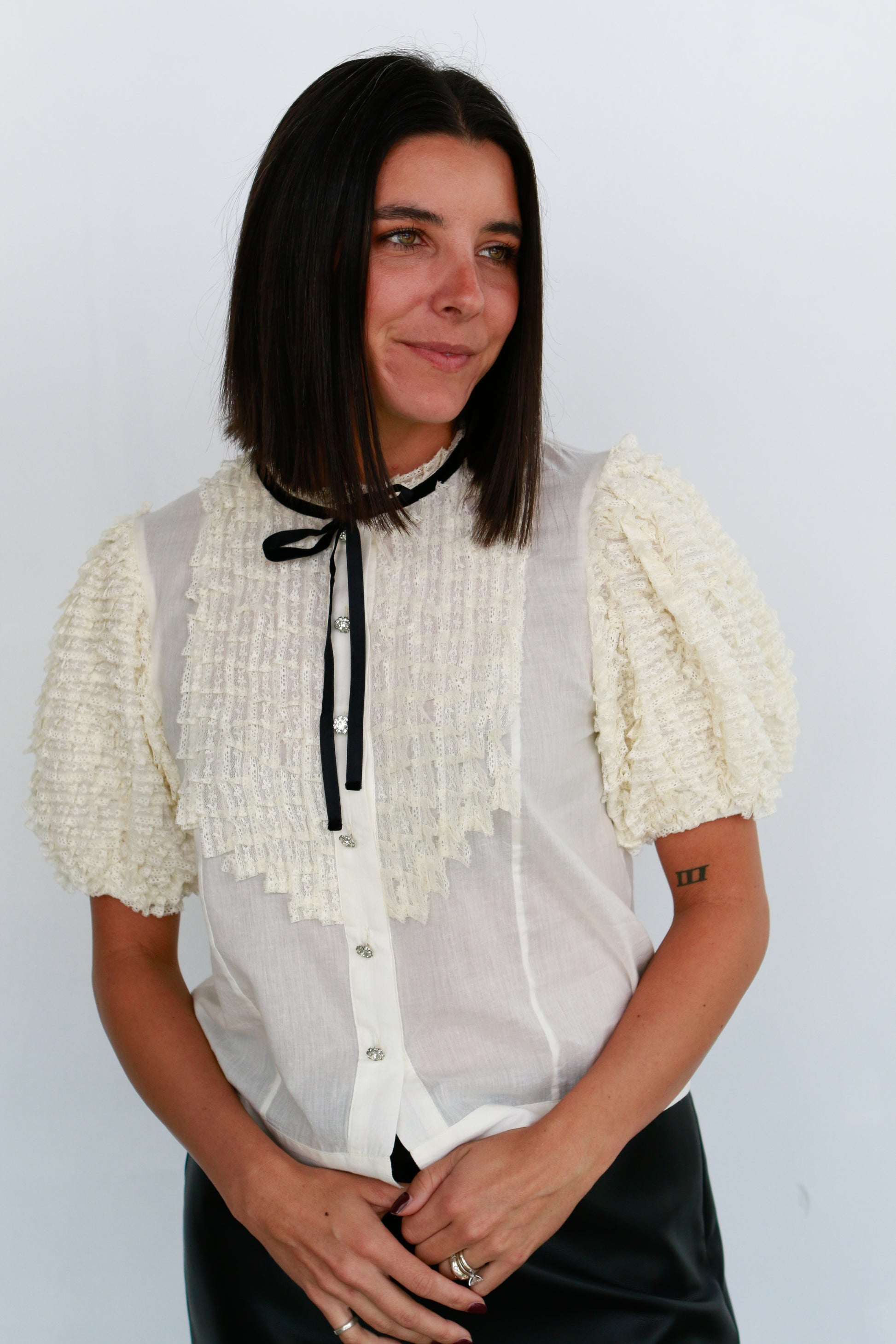 Woman wearing a white blouse with ruffled sleeves against a plain background Love the Label
