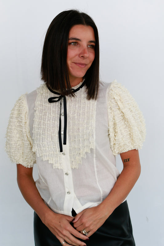 Woman wearing a white blouse with ruffled sleeves against a plain background Love the Label