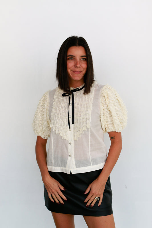 Woman wearing a white blouse with lace details and a black skirt against a white background