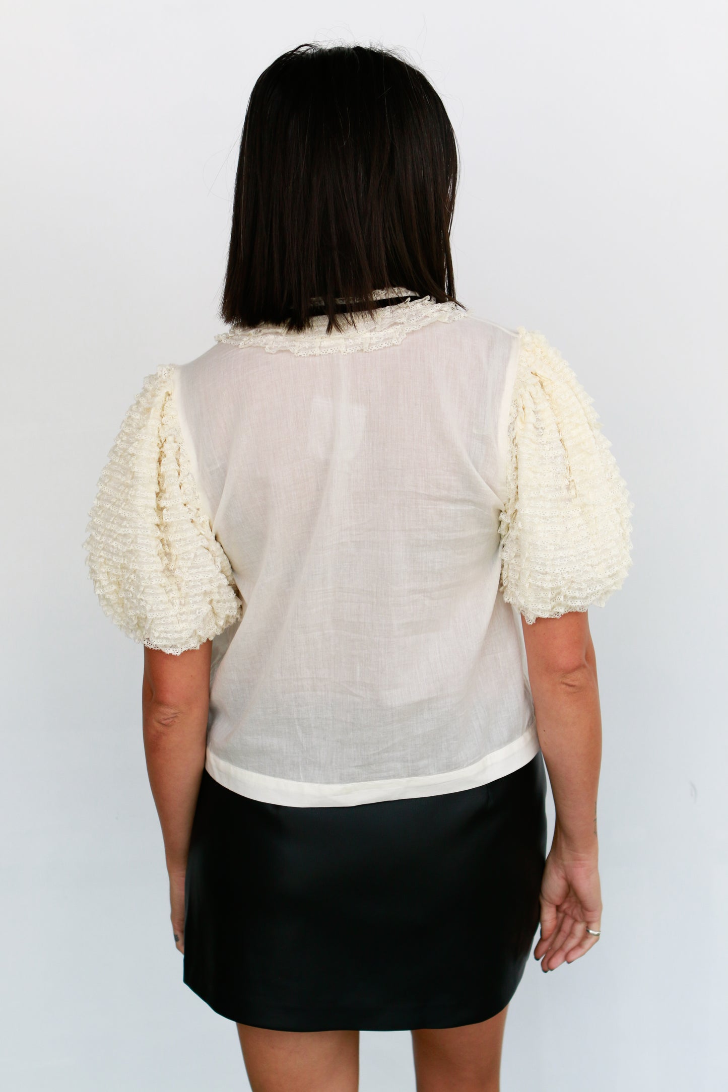 Person wearing a light-colored blouse with puffed sleeves and a black skirt on a white background