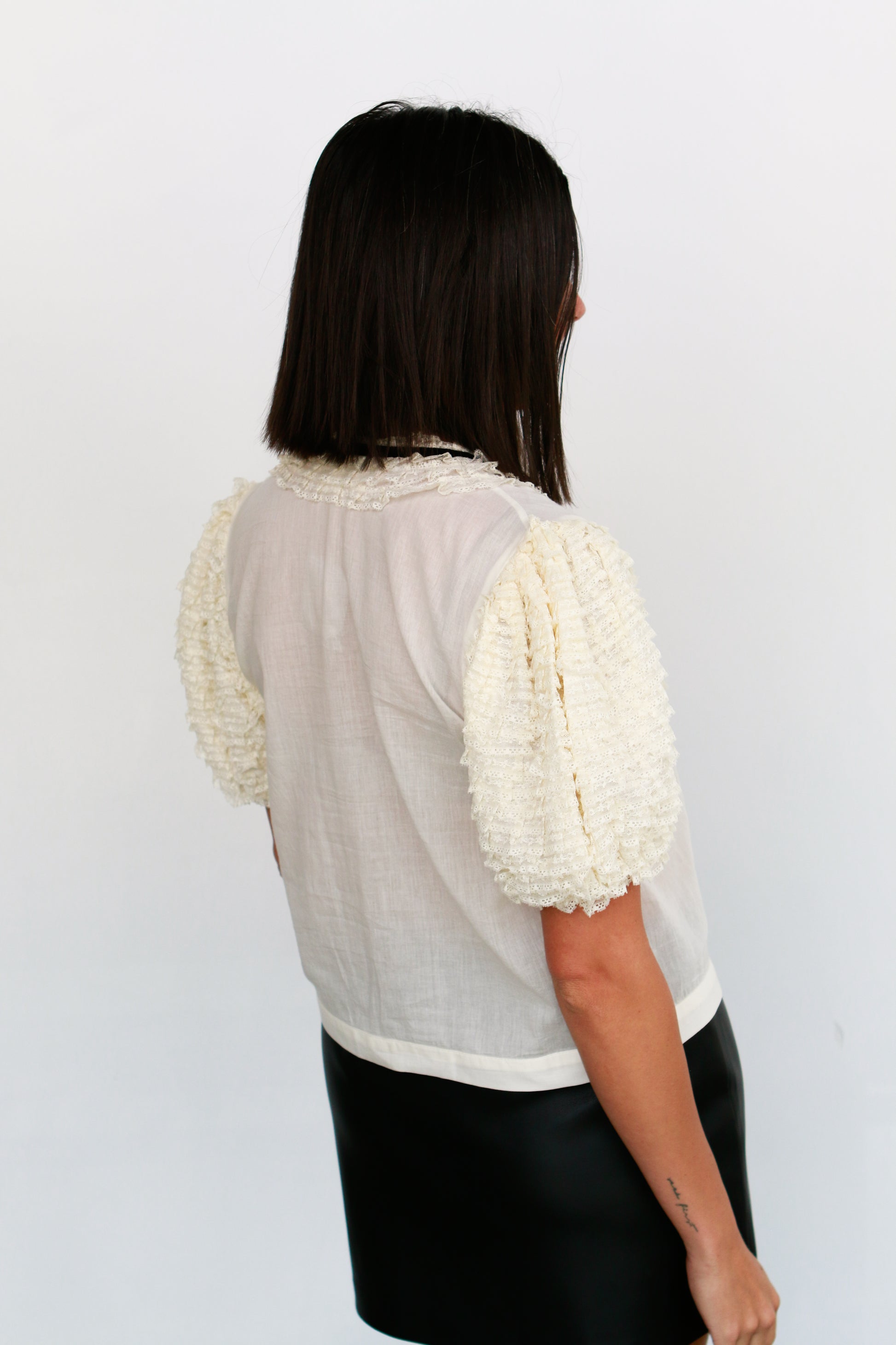 Woman wearing a light-colored blouse with ruffled sleeves against a white background