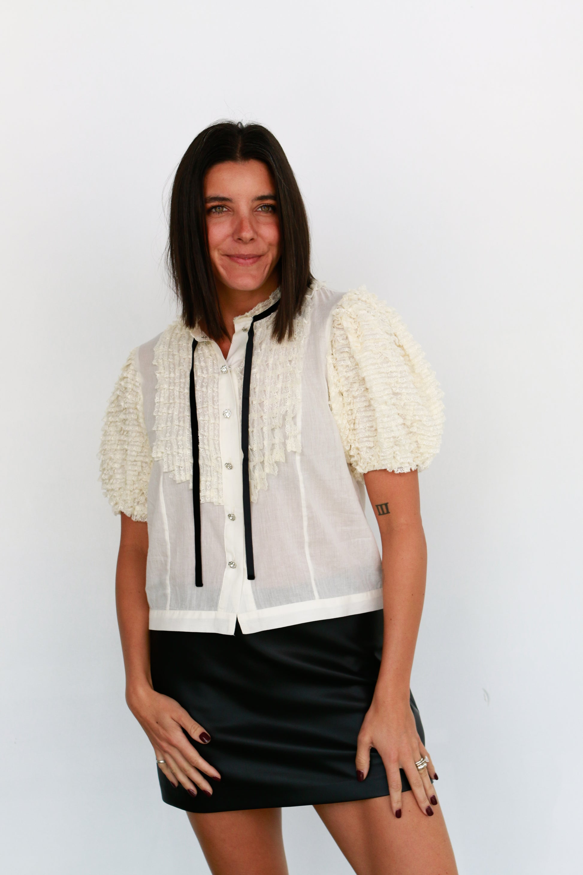 Woman wearing a white blouse with lace sleeves and a black skirt against a plain background