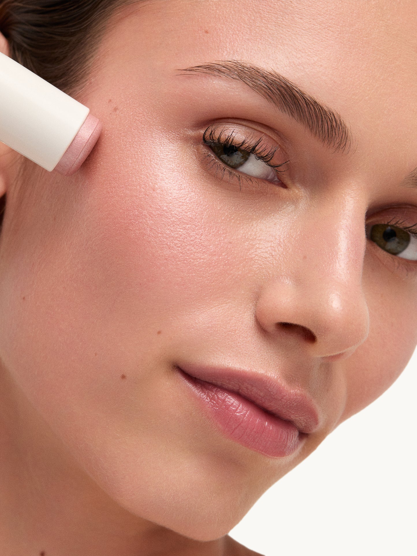 Close-up of a woman applying makeup with a concealer stick on a white background