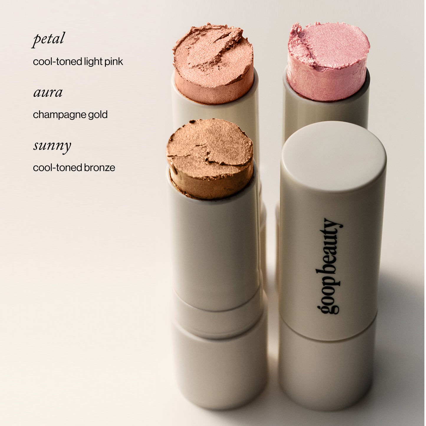 Three cosmetic sticks with different colored tops on a light background, featuring the brand 'goopbeauty'.